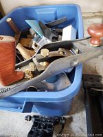 Overhead view of plastic bin filled with hand planes, goggles, chisels and gouge