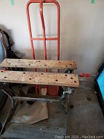 Workmate workbench with wooden top slats and metal frame next to dolly.