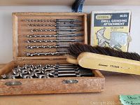 Wooden box with drill bit set, cardboard box for drill grinding attachment, two hand brooms with wooden handles.