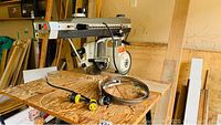 Radial arm saw with some accessories like cords laid on wooden bench.