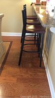 Side view of three bar stools lined up at a kitchen counter showing black metal frame and reddish-brown wood seats.