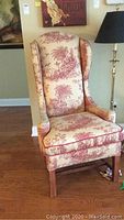 Full frontal view of wingback chair showing shape, upholstery pattern and wooden legs.