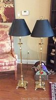 Photo of two matching brass floor lamps with black shades positioned next to an armchair, showing overall height and base details.