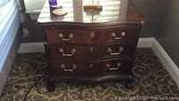 Front view of three-drawer nightstand showing curved front, scalloped top edge and claw and ball feet
