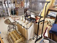 Photo showing a black metal frame laundry hamper with four beige fabric bags and two metal shoe racks in cream and brown color in basement setting.