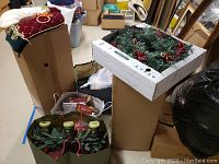 Overall view of multiple boxes with Christmas decorations including greenery candle holders, boxed artificial pre-lit tree.