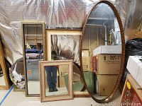 Six framed mirrors leaning against a wall in a basement setting, showing different sizes and frame styles.