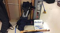 Photo of black, brown, and natural wooden baseball bats and JumpSnap jump rope system box beside a blue folded chair in carrying bag.