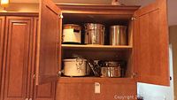 Stock pots, steamers and slow cooker stored in a wooden cabinet.