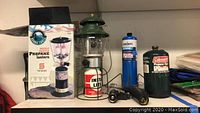 Full view of both propane lanterns, boxed Ozark Trail lantern, Bernzomatic propane tank with nozzles, and Coleman propane fuel canister on shelf