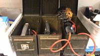 View of three metal tool boxes, two containing power tools with visible orange cords.