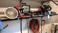 Shelf displaying Black & Decker Fire Storm drill, Black & Decker cordless broom, hedge trimmer, shop lights, and extension cords.