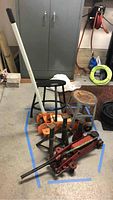 Full view showing three hydraulic jacks, two jack stands, and two stools on garage floor.