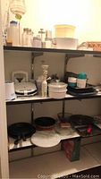 Shelves with various kitchen bakeware including glass pie plates, casserole dishes, pans, and kitchen appliances like Braun appliance and sandwich press.