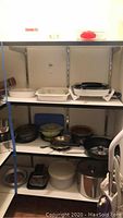 Shelf with a variety of pots, pans, covered stoneware dish, and electric skillet with glass lid.