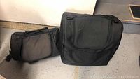 Two black motorcycle bags on the floor, one larger and one smaller, showing overall condition and structure of the bags.