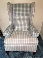 Front view of blue plaid wingback chair with matching bolster and square pillow on blue carpet.