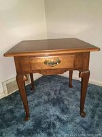 Front view of the Ethan Allen end table showing the single drawer and curved legs on carpeted floor.