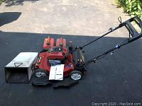 Full view of Toro 22-inch lawn mower with bagger attachment and two gas cans beside it on a paved driveway.