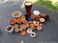 Wide view of all planting containers arranged on the pavement showing different sizes and types including terracotta, stoneware, ceramic and glass pots.