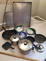 View showing assortment of cookware including metal baking sheets, ceramic frying pans, pots with lids, and grill pans.