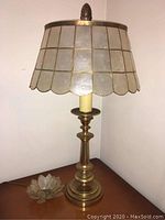 Full view of brass lamp with shell shade on table showing base and shade details.