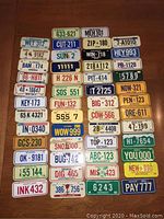 Array of 50 miniature license plates arranged on a wooden surface, showing a variety of US states and slogans.