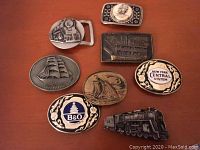Photo showing all 9 assorted railroad and ship-themed belt buckles arranged on a wooden surface.
