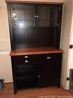 Full front view of the kitchen cupboard and hutch showing two drawers, glass-paneled upper doors, open shelving, and lower cabinet doors.