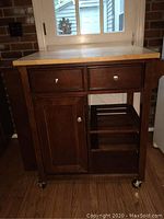 Front view of dark wood kitchen island cart with two drawers, cabinet door, and open shelves on caster wheels.