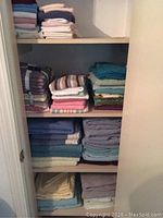View of multiple shelves in a closet with stacks of towels in different colors, sizes, and patterns.