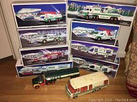 Eight boxed Hess trucks visible stacked showing different truck models with Hess branded packaging artwork.