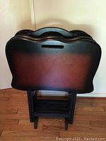Front view of four dark brown wooden tray tables nested together in their matching stand showing curved edges and built-in handles.