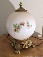 Front angle of glass lamp showing brass base and hand-painted leaf design on shade