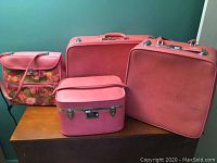 Set of four pink vintage Ventura luggage items arranged on wooden surface with one floral shoulder bag and three luggage cases