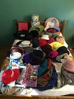 Wide shot of all vintage hats, scarves, hat boxes and stands laying on table and wooden chair backs in background