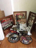 Overview of lot showing framed bar mirrors, shirts, sweatshirt, box of coasters, and decorative trays on floor