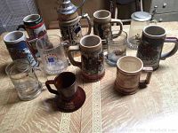 Overview of 11 assorted steins and mugs on table showing variety of ceramic and glass pieces