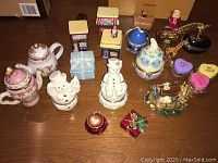 Wide view of assortment of small decorative trinket boxes including teapot, snowmen, houses, hearts and animal shaped boxes on wooden surface.