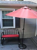 Metal patio glider with red cushion and red umbrella outside on a wooden deck.