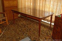 Full length side view of the walnut finish wood dining table with glass top, showing slender tapered legs and rectangular shape.