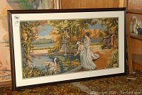 Full view of framed needlepoint artwork resting against a wall, showing the entire scene and frame.