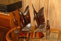 Four wooden animal statuettes on glass table: two large fish/billfish, one medium bird, one small bird figurine.
