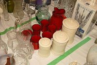 Photo showing assorted clear glass pitchers, red pitcher with matching glasses, and beige ceramic canisters.
