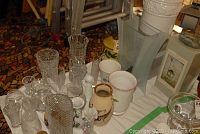 Photo showing clear glass vases and assorted pottery and ceramic vases with floral designs on a table.