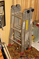 Front view of Featherlite combination ladder folded and standing upright showing red rubberized feet and adjustable locking knobs.