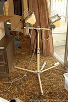 Full view of the set of two construction lights mounted on tripod stand in a room with patterned carpet.