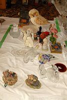 Photo showing assorted decorative figurines including a ceramic owl with textured fur, two pink flamingo figurines, small angel and child ceramic figurines, clear glass plates and bowls, and painted ceramic birdhouse.
