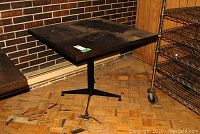 Full view of square table showing black melamine top and metal base on parquet floor.