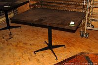 View of rectangular table with melamine top and black metal base on parquet floor, showing surface wear and scratches.